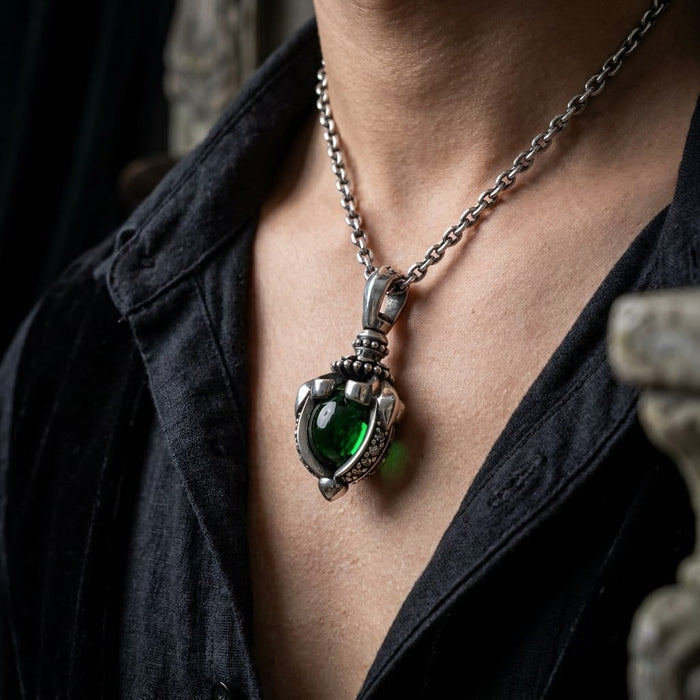 Close-up of a person wearing a chunky sterling silver gothic pendant featuring a large, dark green moonstone in a tribal claw setting, worn on a silver chain with an open black shirt.