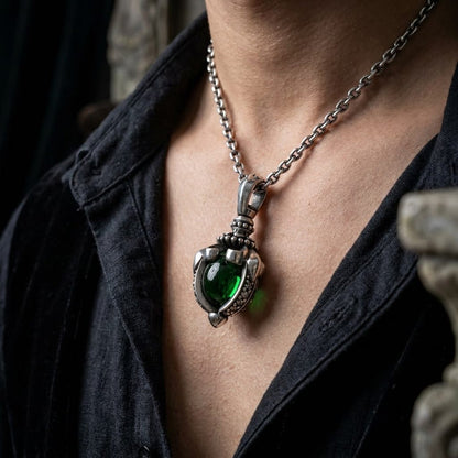 Close-up of a person wearing a chunky sterling silver gothic pendant featuring a large, dark green moonstone in a tribal claw setting, worn on a silver chain with an open black shirt.