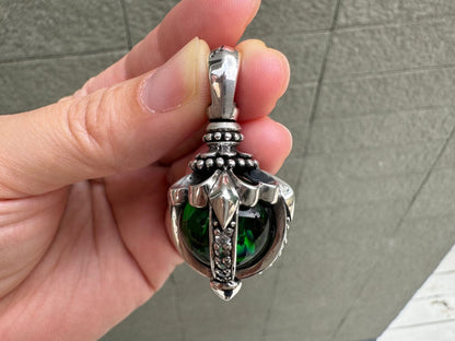 Ornate beaded bail and gothic sterling silver claws encasing the deep green moonstone, displayed between fingers.
