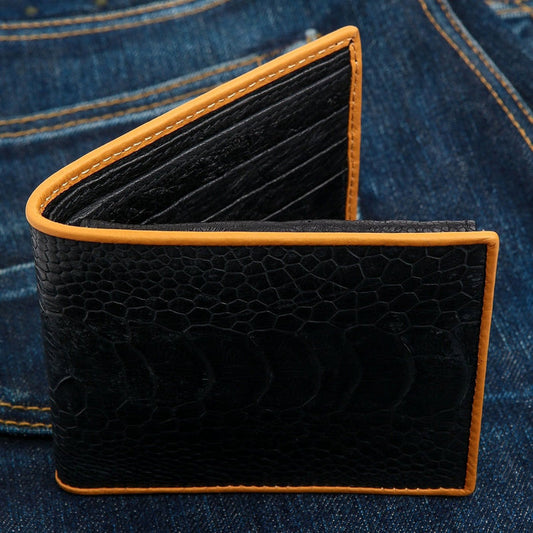 The black genuine ostrich leg wallet with tan trim, sitting on a pair of blue jeans.