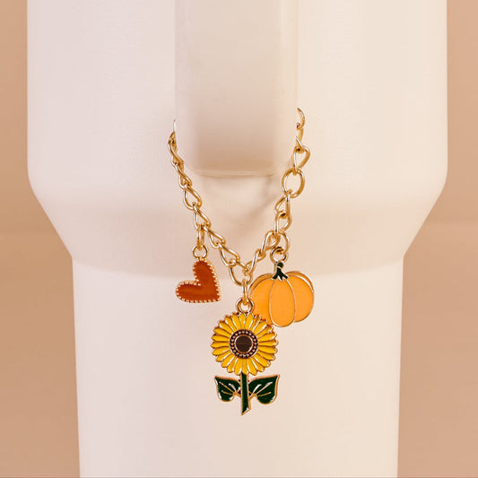 The Darling Effect’s Happy Harvest Tumbler Charm features a gold chain with sunflower, orange heart, and pumpkin charms—an ideal cream-colored accessory to bring fall vibes to your tumbler.