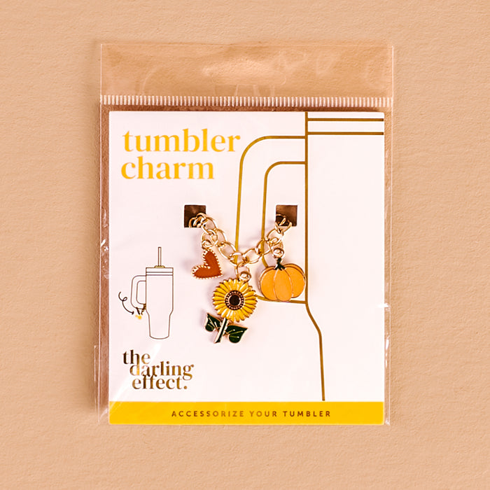 The Darling Effect Happy Harvest Tumbler Charm features a gold chain with sunflower, pumpkin, and heart charms, displayed on a labeled card—perfect for bringing fall vibes to your seasonal tumbler accessories.