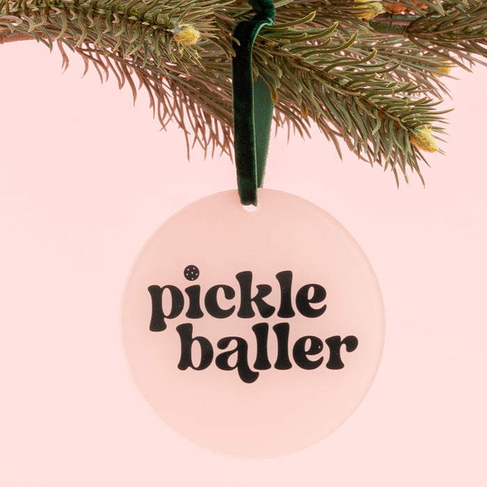 Add a playful touch to your holiday décor with The Darling Effect’s Holiday Tree Ornament - Pickleballer, featuring bold black “pickle baller” text on a light pink background. This round acrylic ornament hangs from a pine branch with a green ribbon and makes the perfect festive statement for pickleball fans this season.