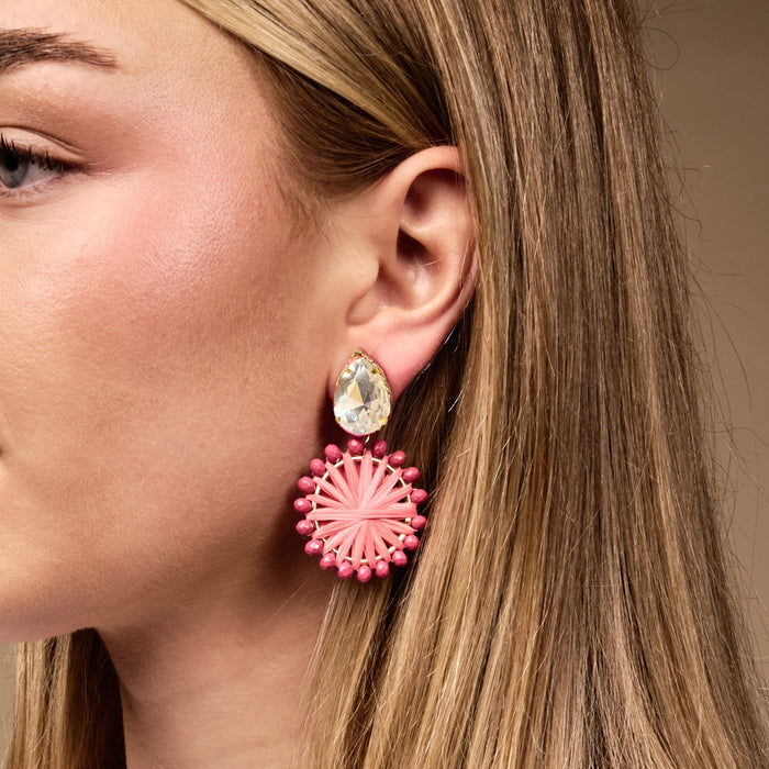 A woman wears The Darling Effect’s Hot Pink Radiant Gem Earrings: lightweight, boho gold earrings with a teardrop clear gem and a dangling hot pink raffia circle, perfect for everyday wear.
