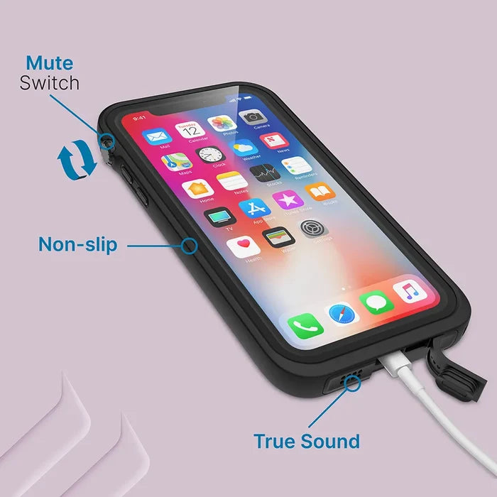 An iPhone Xs Max in a black Catalyst Case US waterproof case, shown with attached charging cable. Blue labels highlight the "Mute Switch" by the side button, "Non-slip" case edge, and "True Sound" near the bottom speaker. Light purple background.