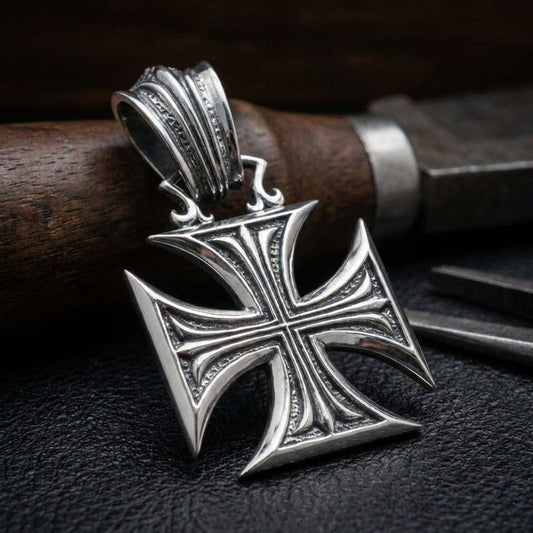 Sterling silver Iron Cross pendant with ornate detailing and decorative bail, displayed on black leather surface with wooden handle knife in background, featuring vintage Gothic style design with concave arms and textured border accents
