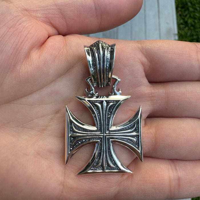 Hand holding sterling silver iron cross pendant showing size and gothic textured background