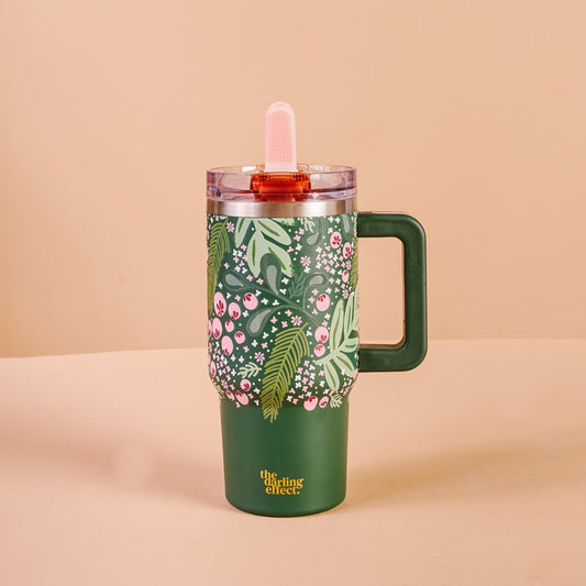 The Darling Effect's Jolly Sprig 20 oz Lifestyle Flip Straw Tumbler is green with pink and white floral designs, green leaves, triple-walled insulation, a clear lid, a pink straw, and "The sassy effect" in yellow at the bottom.