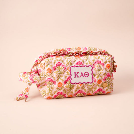 The Darling Effect's Kappa Alpha Theta Essentials Quilted Cosmetic Pouch features a floral pattern, zipper, side tie, and Greek letters ΚΑΘ on a white and pink patch—ideal for sorority essentials with its soft beige background.