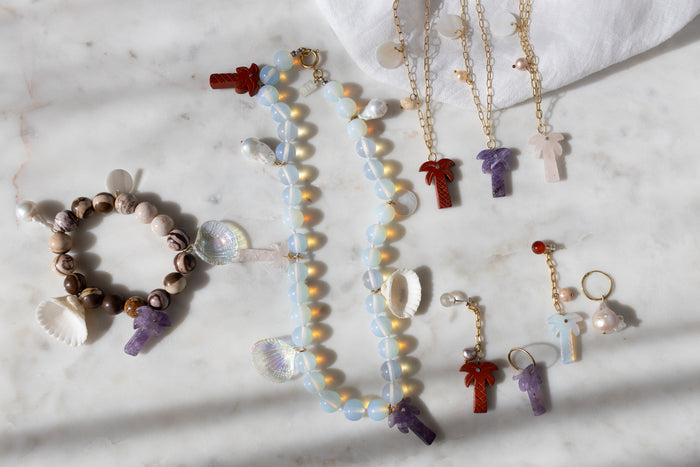 WALD Berlin's Mexicana La Bamba Bracelet is displayed on marble alongside beaded jewelry, featuring bracelets, necklaces, and earrings with shell, pearl, palm tree, and gemstone pendants.