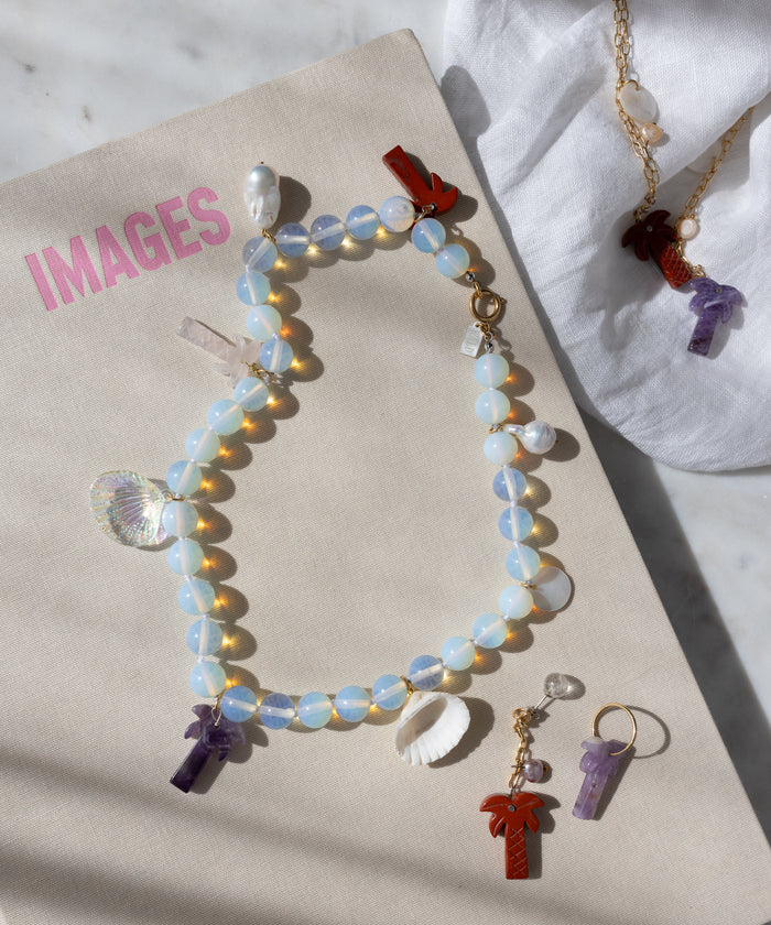 The WALD Berlin Mexicana La Bamba Necklace features opalite beads, shell, crystal, and red pendants. Shown atop a book labeled "IMAGES," it's paired with matching gemstone pendant necklace and earrings on white cloth.