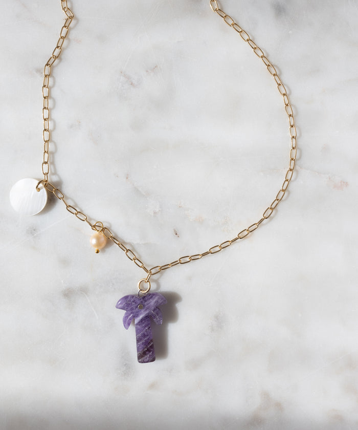 WALD Berlin’s Mexicana Solo Amore Necklace: a handmade gold-plated piece with a white circular charm, yellow bead, and purple hand-carved stone palm pendant, elegantly displayed on white marble.
