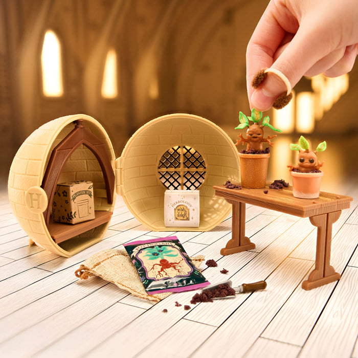 Miniature garden setup with small plants and a hand interacting with it on a wooden floor.