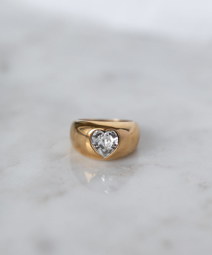 The WALD Berlin Mom Swarovski Heart Ring, adorned with a sparkling heart-shaped Swarovski stone, rests elegantly on a light marble surface.