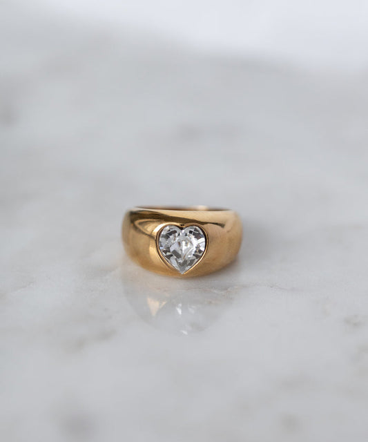 The WALD Berlin Mom Swarovski Heart Ring, adorned with a sparkling heart-shaped Swarovski stone, rests elegantly on a light marble surface.