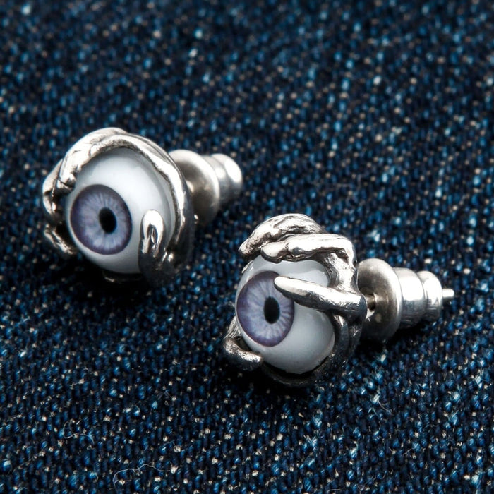 A pair of handmade monster eye stud earrings with intricately detailed silver claws and realistic purple eyes.