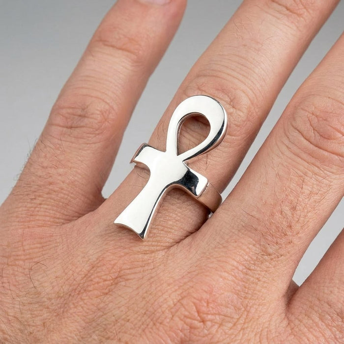Hand wearing a polished silver ankh ring on a plain background.