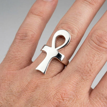 Hand wearing a polished silver ankh ring on a plain background.