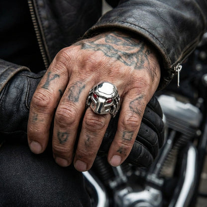 Silver Predator-inspired skull ring with red accent details worn on a tattooed hand resting on a motorcycle, featuring a rugged biker aesthetic with black leather jacket