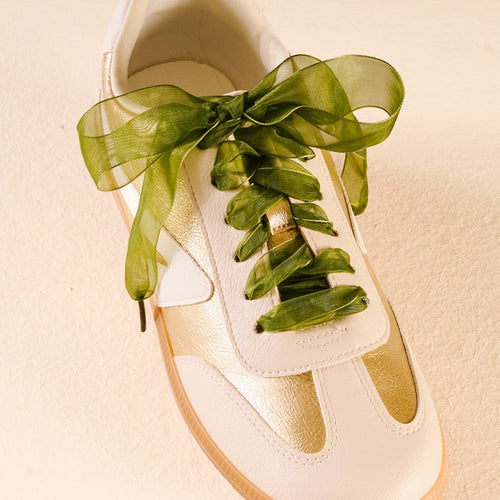 A white and gold sneaker with Sheer Green Step It Up Shoelaces from The Darling Effect, tied in a neat bow.