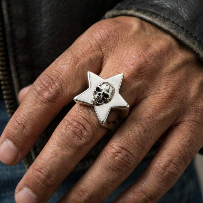Sterling silver gothic skull star ring worn on middle finger of man's hand, featuring detailed skull centerpiece on six-pointed star design, paired with leather jacket and denim for edgy biker style
