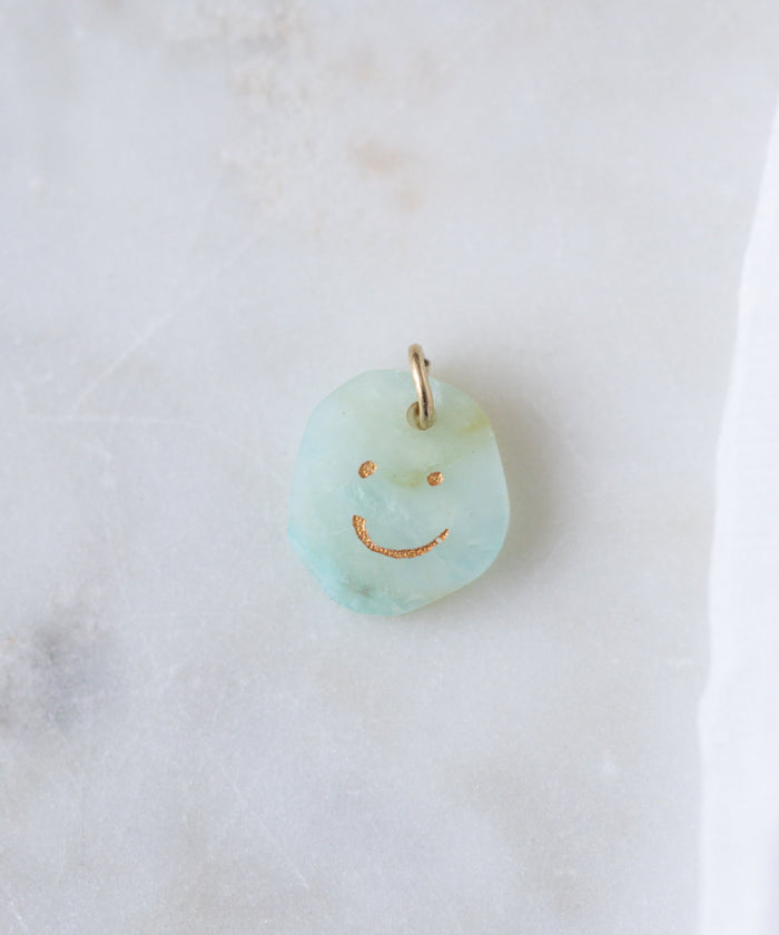 The WALD Berlin Smilie Dude Gemstone Pendant Without Chain features a light blue real gemstone, gold smiley face engraving, and a small metal loop, shown on a white marble surface.