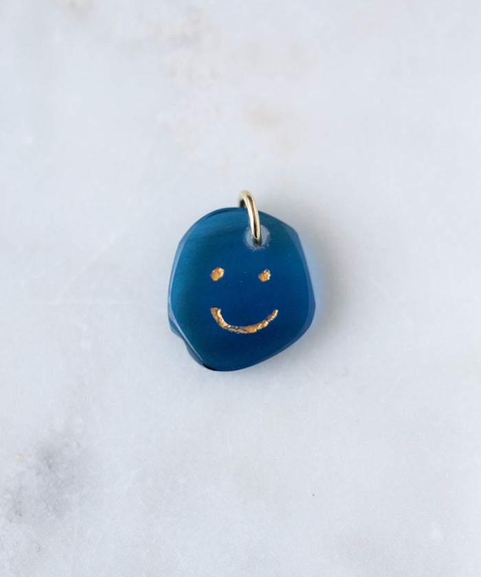 The WALD Berlin Smilie Dude Gemstone Pendant Without Chain features a small blue charm with a gold smiling face and metal loop, made in Germany—an elegant accent for any 18k gold necklace.