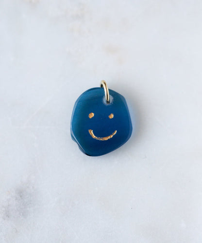 The WALD Berlin Smilie Dude Gemstone Pendant Without Chain features a small blue charm with a gold smiling face and metal loop, made in Germany—an elegant accent for any 18k gold necklace.