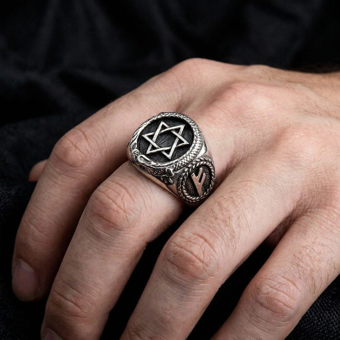 Silver Star of David signet ring worn on a hand against a dark background.