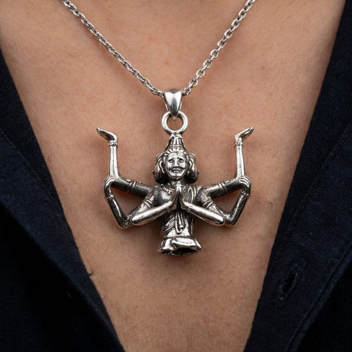 Lifestyle view of the silver four-faced deity pendant worn on a chain, resting on a model's chest over a dark shirt.