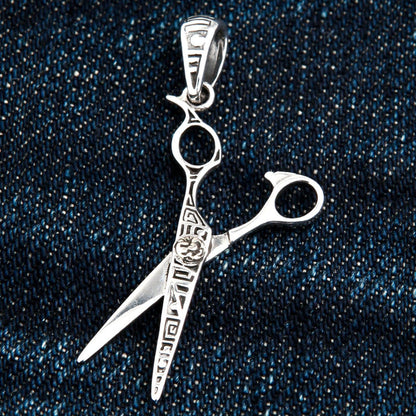 A close-up of the sterling silver scissors pendant on a dark denim background.
