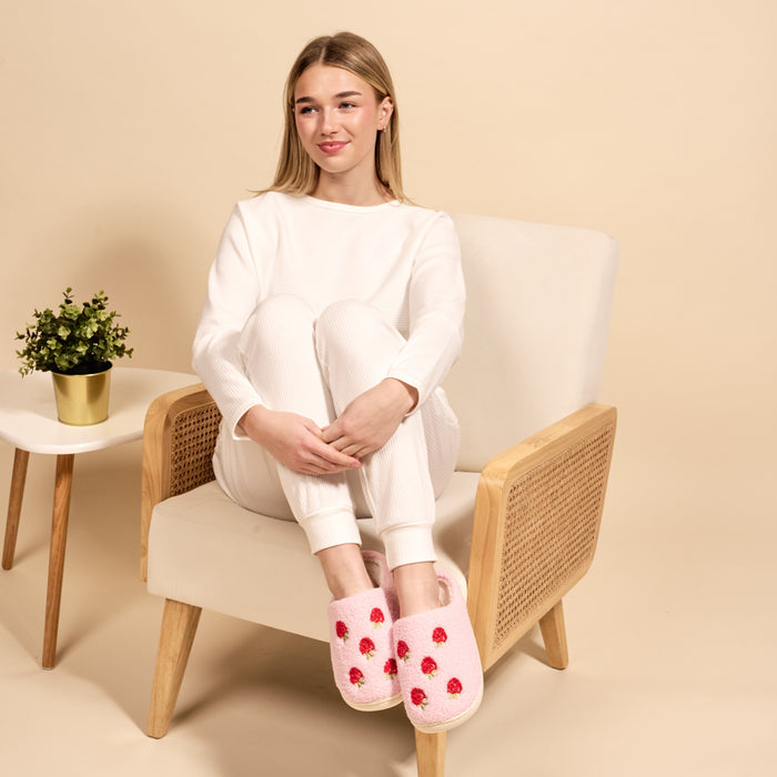 A young woman with blonde hair sits in a chair wearing white pajamas and The Darling Effect's Strawberries Fuzzy Slippers.