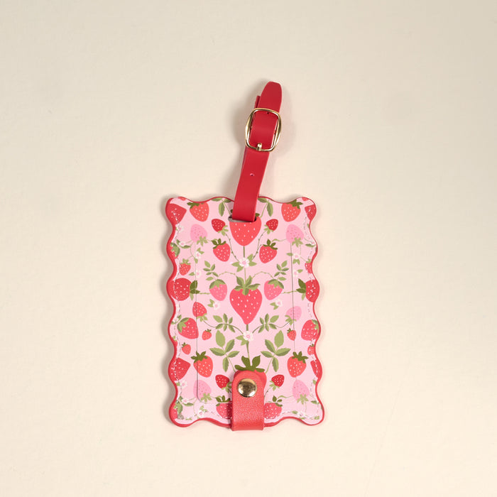 The Darling Effect’s Strawberry Fields Jetsetter Luggage Tag features a pink scalloped edge, red strawberries, green leaves, a privacy flap, and a red strap with gold buckle—an adorable travel accessory.