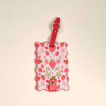 The Darling Effect’s Strawberry Fields Jetsetter Luggage Tag features a pink scalloped edge, red strawberries, green leaves, a privacy flap, and a red strap with gold buckle—an adorable travel accessory.