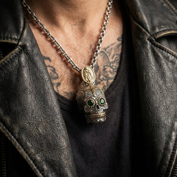 Intricately detailed silver sugar skull pendant with green gemstone eyes and gold Virgin Mary medallion on heavy chain, worn by tattooed man in black leather jacket