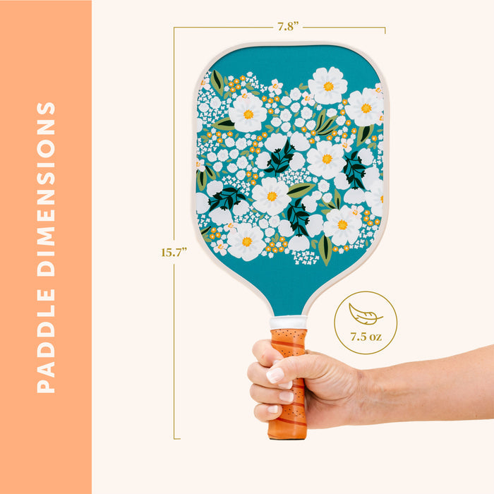 A hand holds The Darling Effect's Sweet Meadow Green Pickleball Paddle, featuring a teal background with white flowers. Text shows it is 15.7" long, 7.8" wide, and weighs 7.5 oz, with "Paddle Dimensions" displayed vertically on the left.