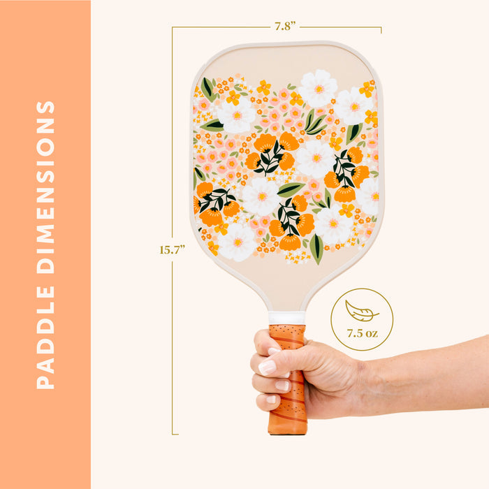 A hand holds The Darling Effect’s Sweet Meadow Tan Pickleball Paddle—ideal for pickleball fans. "Paddle Dimensions" on an orange strip highlights: 15.7" long, 7.8" wide, and weighs only 7.5 oz.