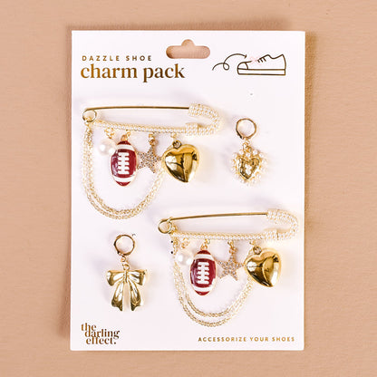 The Darling Effect’s Tailgate Time Dazzle Shoe Charm Pack features two gold safety pin-style sneaker charms with pearl chains, a red football, gold heart, star, pearl, heart pendant, and bow—fun accents to upgrade your footwear.