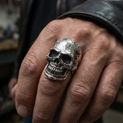 A man's hand wearing the large tough head skull ring, showcasing its rugged, battle-worn texture.