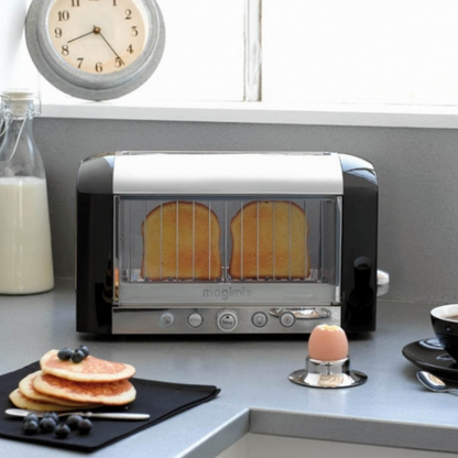 Black magimix vision toaster toasting bread on a grey counter next to an egg and pancakes