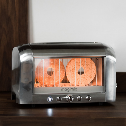 A chrome magimix vision toaster toasting bagels on a dark wooden counter