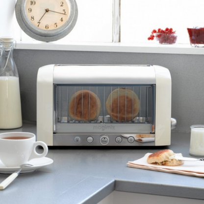 A cream magimix vision toaster toasting english muffins on a grey kitchen counter next to milk and tea