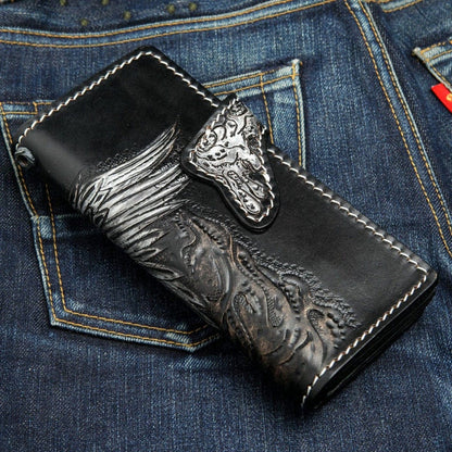 Handcrafted leather skull wallet with ornate dragon head snap closure and carved wing design on blue jeans
